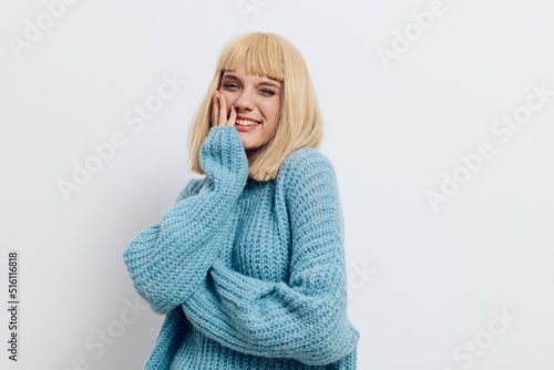 horizontal photo on a light background, of a pleasant woman in a light blue sweater, smiling broadly and looking at the camera with her hands near her face © Tatiana