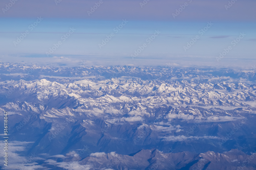 Window view from an airplane on the snow capped mountain ranges of the Alps at the border Austria Italy, Europe, EU. High peak are shrouded in clouds. Flying high above the ground. Freedom