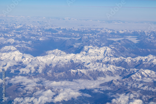 Window view from an airplane on the snow capped mountain ranges of the Alps at the border Austria Italy, Europe, EU. High peak are shrouded in clouds. Flying high above the ground. Freedom © Chris