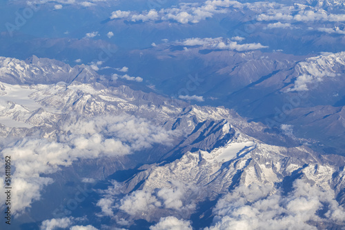 Window view from an airplane on the snow capped mountain ranges of the Alps at the border Austria Italy, Europe, EU. High peak are shrouded in clouds. Flying high above the ground. Freedom