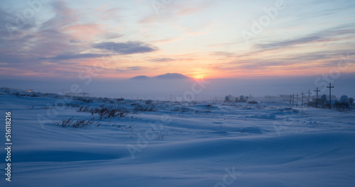 Winter arctic landscape. Sunset in the tundra. Early winter twilight. Cold frosty winter weather. Electric poles and satellite dishes in the snowy tundra. Chukotka  Siberia  Far East of Russia  Arctic