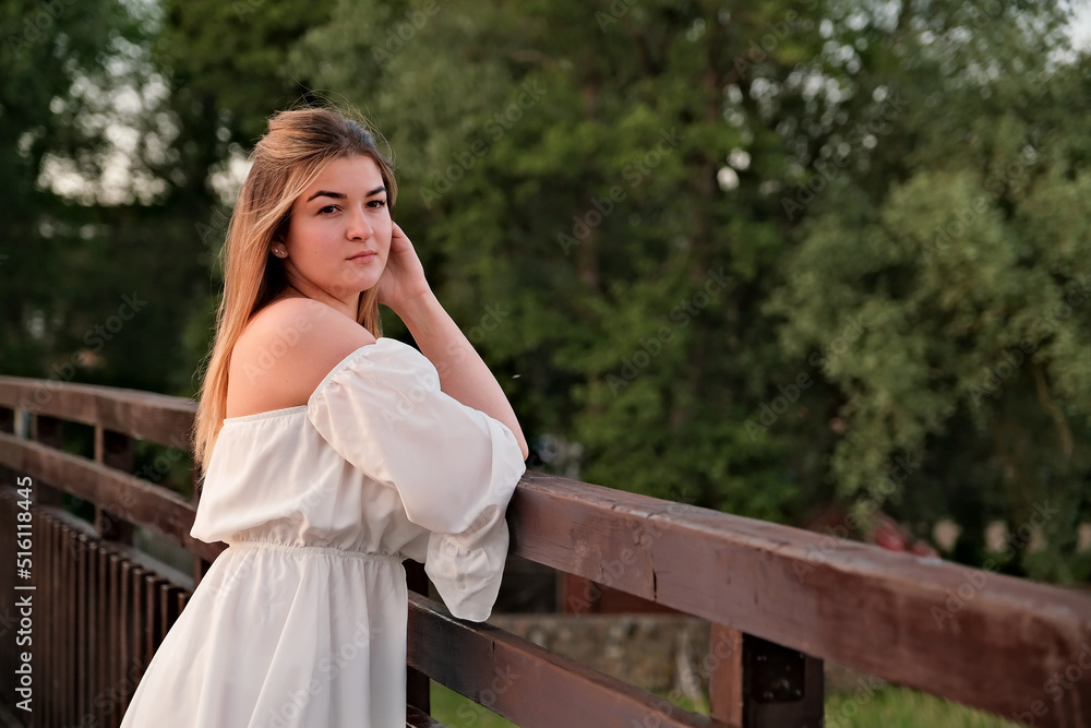 Naklejka premium a beautiful girl in a white dress stands on a wooden bridge.