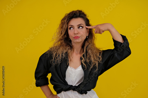Close-up portrait of a beautiful girl on a yellow background. a woman twists her index finger near her temple isolated on a yellow wall. Shocked surprised stunned. positive human emotions