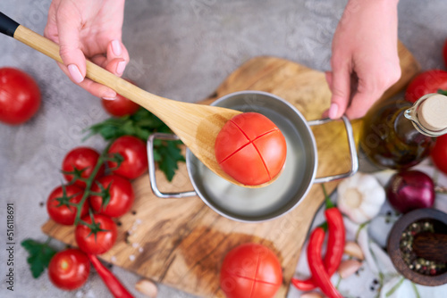 woman blanching a tomato holding over pan with hot water for further peeling photo