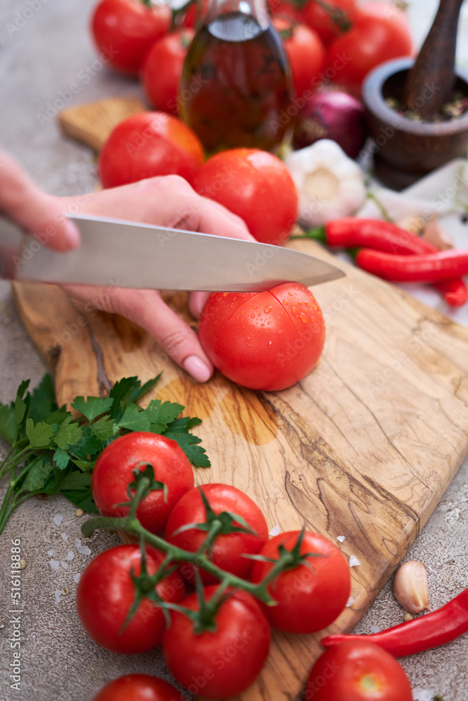 woman making notch on a tomato on wooden cutting board on grey kitchen concrete or stone table woman making notch on a tomato on wooden cutting board on grey kitchen concrete or stone table