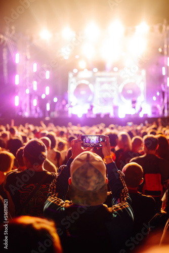 Using a smartphone in a public event, live music festival. Holding a mobile phone in hands and shooting photo or video content. Youth, party, vacation concept. © maxbelchenko