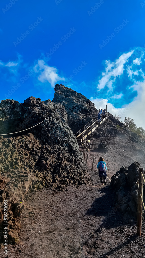 Tourist woman hiking along cloudy edge of active volcano crater of Mount Vesuvius, Province of Naples, Campania region, Italy, Europe, EU. Volcanic landscape full of stones, ashes and solidified lava