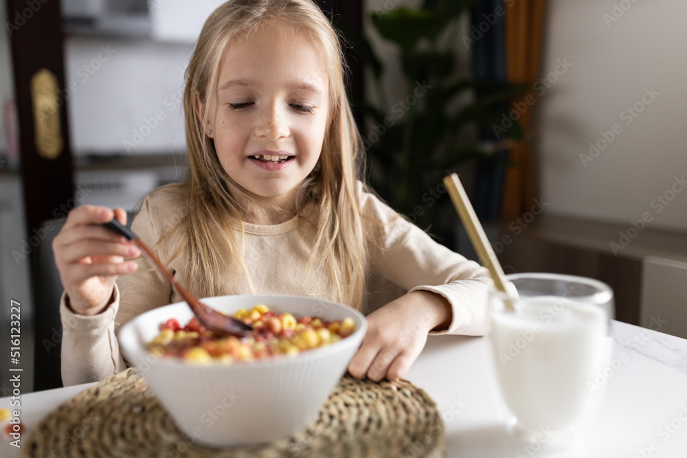 Cute little caucasian girl sitting at table on kitchen early morning and preparing breakfast with colorful cornflakes and milk. Kid enjoying life with healthful food, healthy lifestyle concept Cute little caucasian girl sitting at table on kitchen early morning and preparing breakfast with colorful cornflakes and milk. Kid enjoying life with healthful food, healthy lifestyle concept