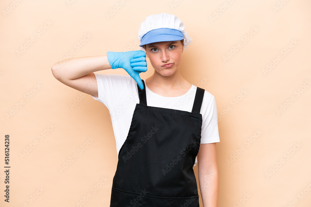 Fishmonger caucasian woman wearing an apron and holding a raw fish isolated on beige background showing thumb down with negative expression Fishmonger caucasian woman wearing an apron and holding a raw fish isolated on beige background showing thumb down with negative expression