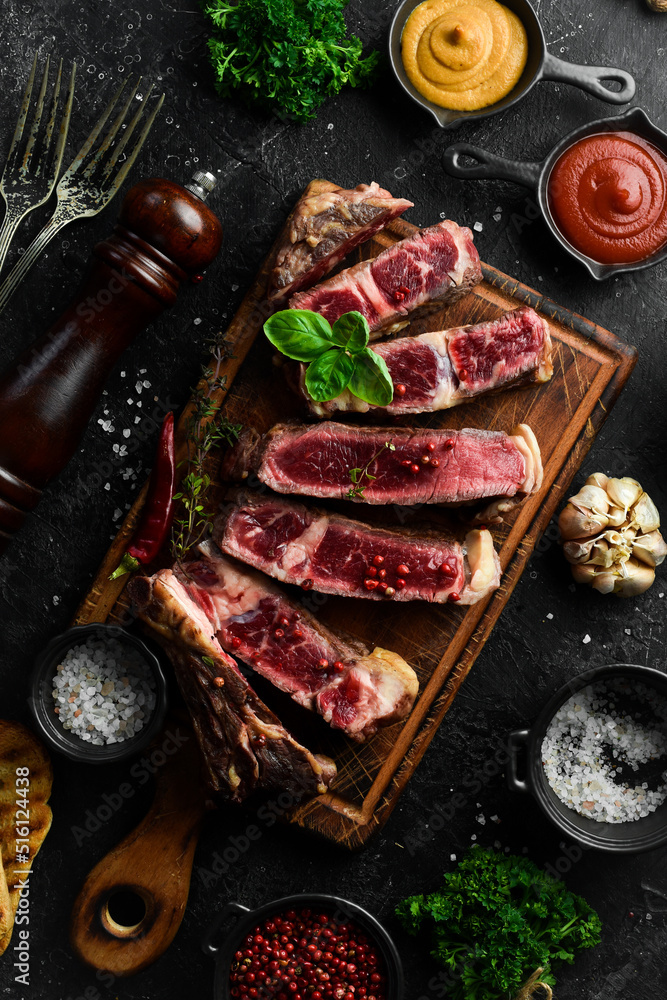 Steak on the bone on the kitchen board. Tomahawk steak on a black wooden background. Top view. Free space for copying. Steak on the bone on the kitchen board. Tomahawk steak on a black wooden background. Top view. Free space for copying.