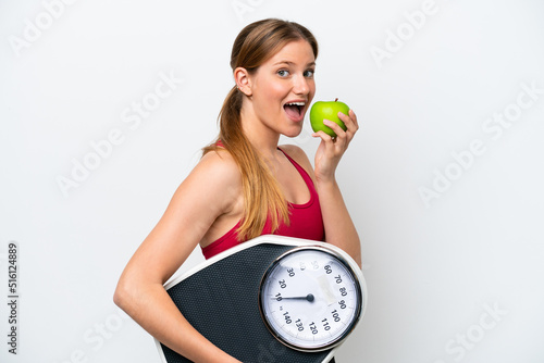 Young pretty blonde woman isolated on white background with weighing machine and with an apple