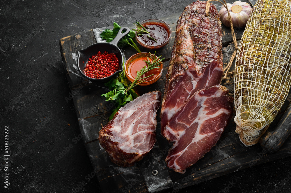 Dried and salted piece of meat. Prosciutto, jamon, on a black stone background. Top view. Free space for text.
