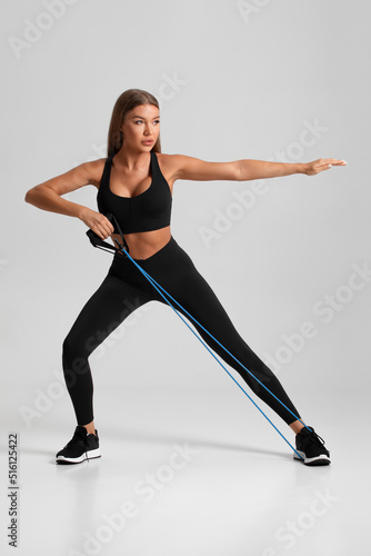 Fototapeta Naklejka Na Ścianę i Meble -  Fitness woman working out with resistance band on gray background. Athletic girl exercises with expander