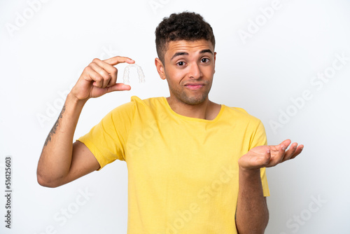 Young Brazilian man holding invisible braces isolated on white background making doubts gesture while lifting the shoulders