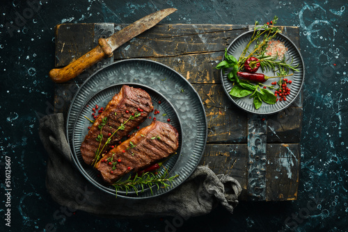 Grilled ribeye beef steak with rosemary, herbs and spices on a dark table. Free space for menus.