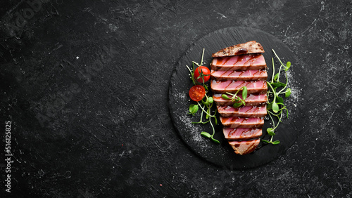 Cooked juicy tuna steak with vegetables on a black stone plate. Restaurant food. Seafood. Rustic style. Flat Lay.