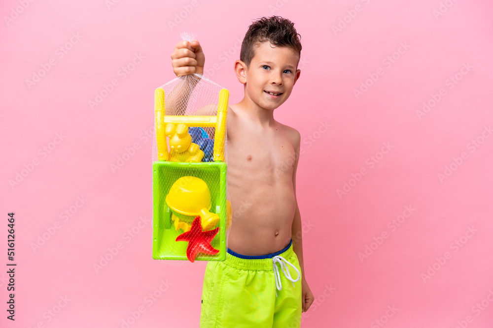 Little caucasian boy holding beach toys isolated on pink background with happy expression Little caucasian boy holding beach toys isolated on pink background with happy expression