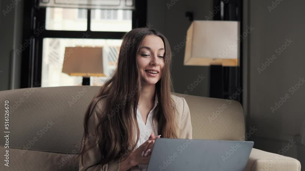 Beautiful businesswoman using laptop for video call online in hotel lounge. Business woman sitting in soft chair calling video chat conference in lobby. Smiling woman making video call business trip. Beautiful businesswoman using laptop for video call online in hotel lounge. Business woman sitting in soft chair calling video chat conference in lobby. Smiling woman making video call business trip.