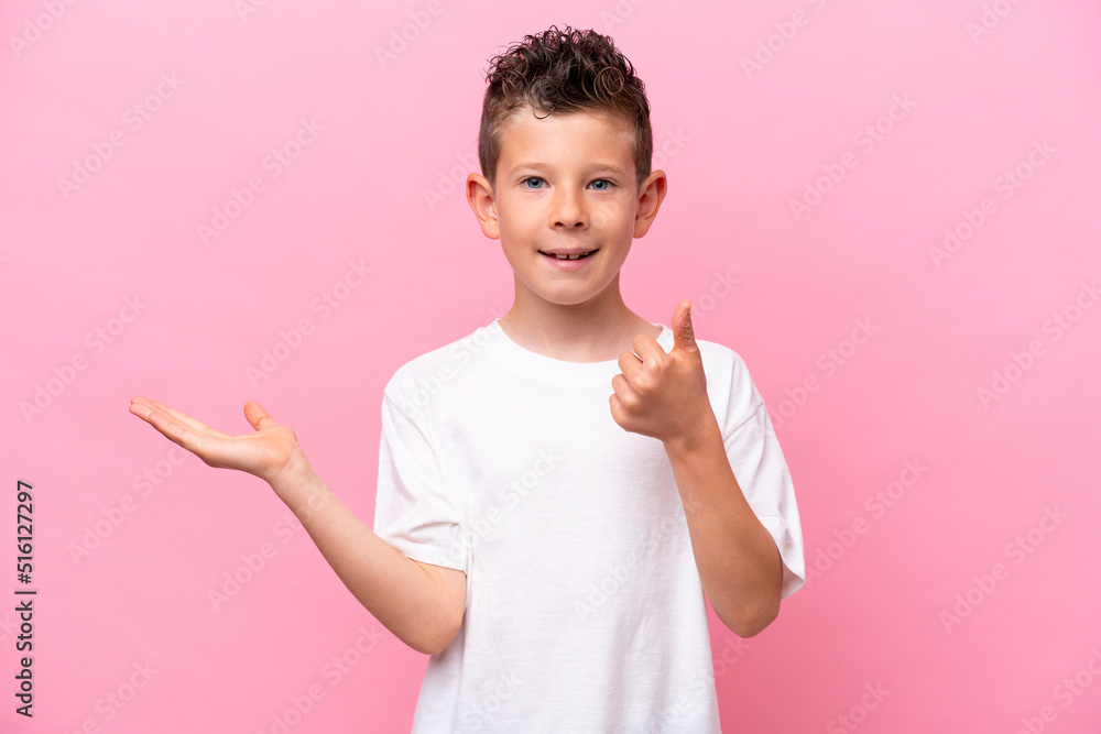 Little caucasian boy isolated on pink background holding copyspace imaginary on the palm to insert an ad and with thumbs up Little caucasian boy isolated on pink background holding copyspace imaginary on the palm to insert an ad and with thumbs up