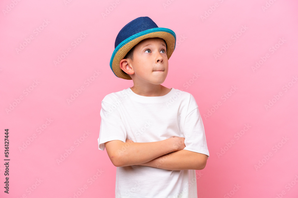 Little caucasian boy wearing a hat isolated on pink background making doubts gesture while lifting the shoulders Little caucasian boy wearing a hat isolated on pink background making doubts gesture while lifting the shoulders