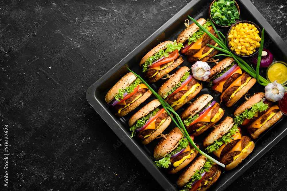 Delicious grilled homemade burgers with beef, tomatoes, cheese, onions and salad. Burger menu. Top view. On a black stone background. Delicious grilled homemade burgers with beef, tomatoes, cheese, onions and salad. Burger menu. Top view. On a black stone background.