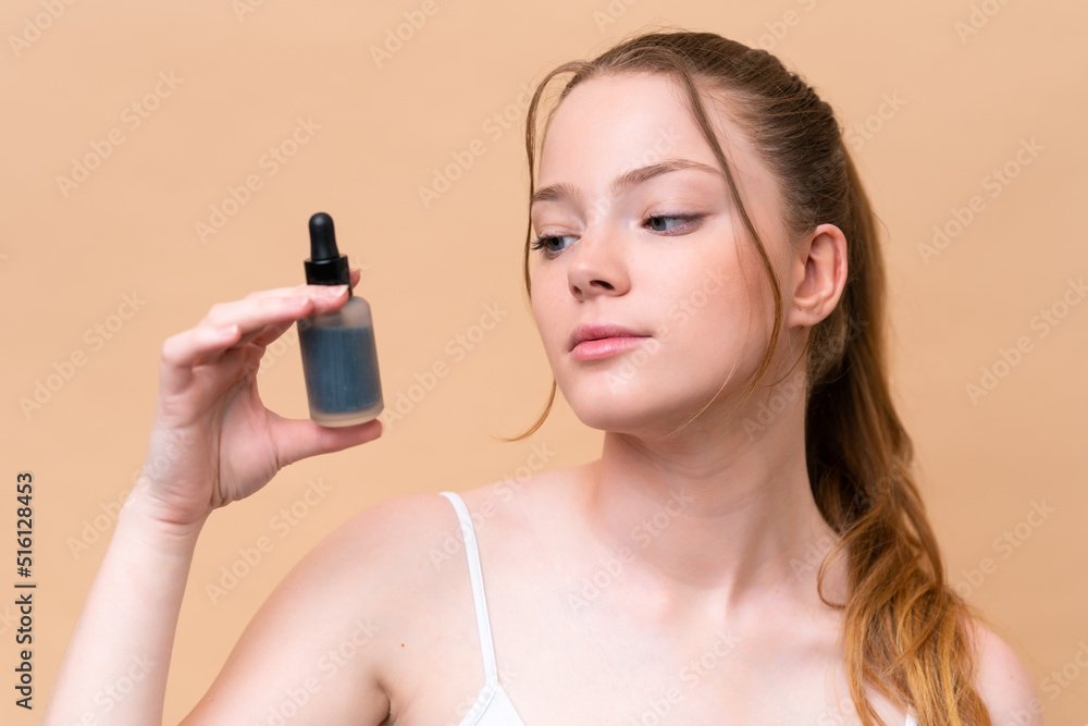 Young caucasian girl isolated on beige background holding a serum. Close up portrait Young caucasian girl isolated on beige background holding a serum. Close up portrait