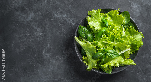 Fresh green salad in a plate of a mixture of green leaves on a dark background. A mixture of healthy greens. The concept of raw food, organic, detox diet.