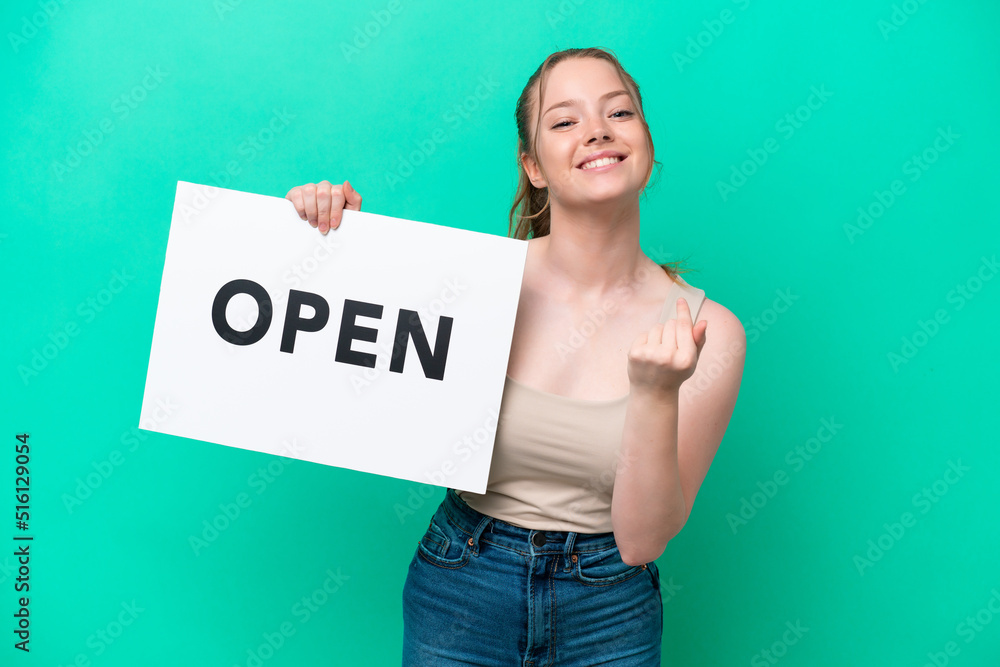 Young caucasian woman isolated on green background holding a placard with text OPEN and doing coming gesture Young caucasian woman isolated on green background holding a placard with text OPEN and doing coming gesture