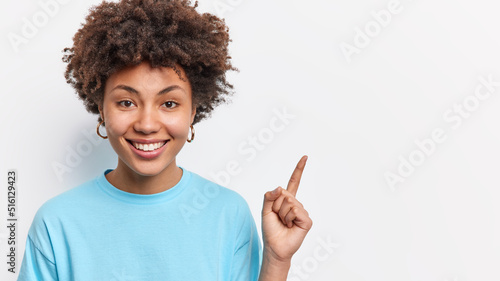 Slika na platnu Pretty smiling young woman points finger on blank space shows advertisement or chart aside wears casual blue t shirt isolated over white background