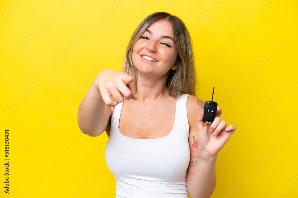 Young woman holding car keys isolated on yellow background points finger at you with a confident expression Young woman holding car keys isolated on yellow background points finger at you with a confident expression