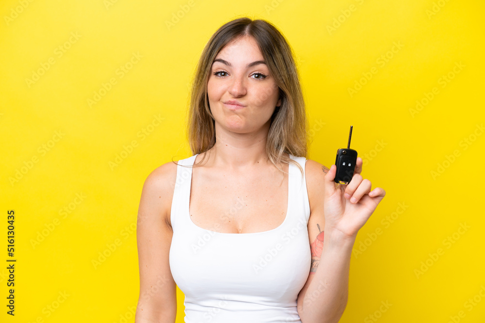 Young woman holding car keys isolated on yellow background with sad expression Young woman holding car keys isolated on yellow background with sad expression
