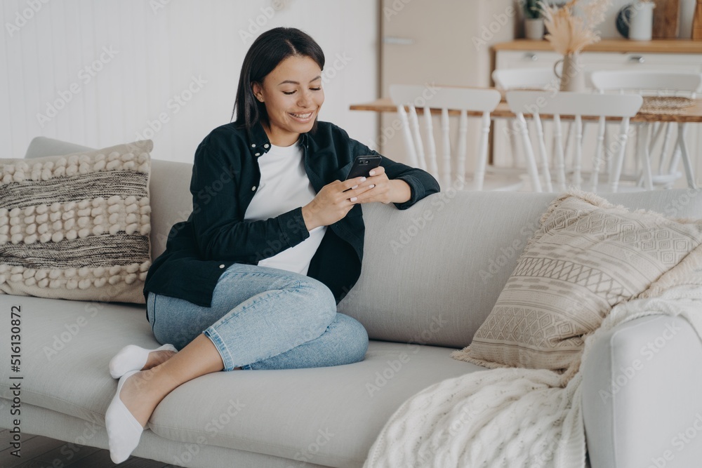 Happy woman relaxing with mobile phone and reading messages on comfortable couch in living room. Happy woman relaxing with mobile phone and reading messages on comfortable couch in living room.
