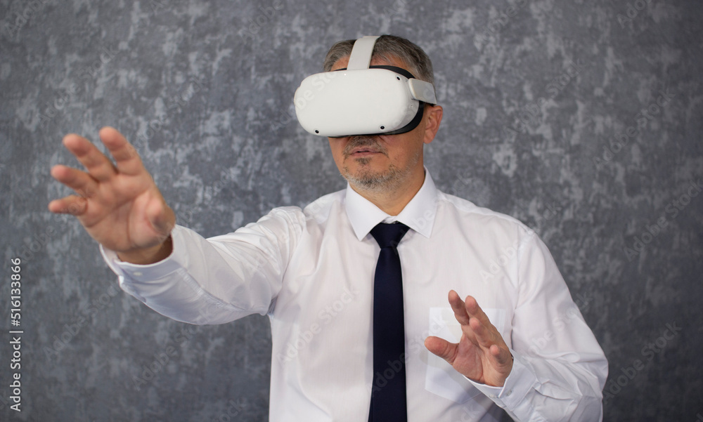 A man wearing virtual reality glasses. A businessman of Caucasian nationality with gray hair, dressed in a virtual reality headset, tie and white shirt. A man wearing virtual reality glasses. A businessman of Caucasian nationality with gray hair, dressed in a virtual reality headset, tie and white shirt.