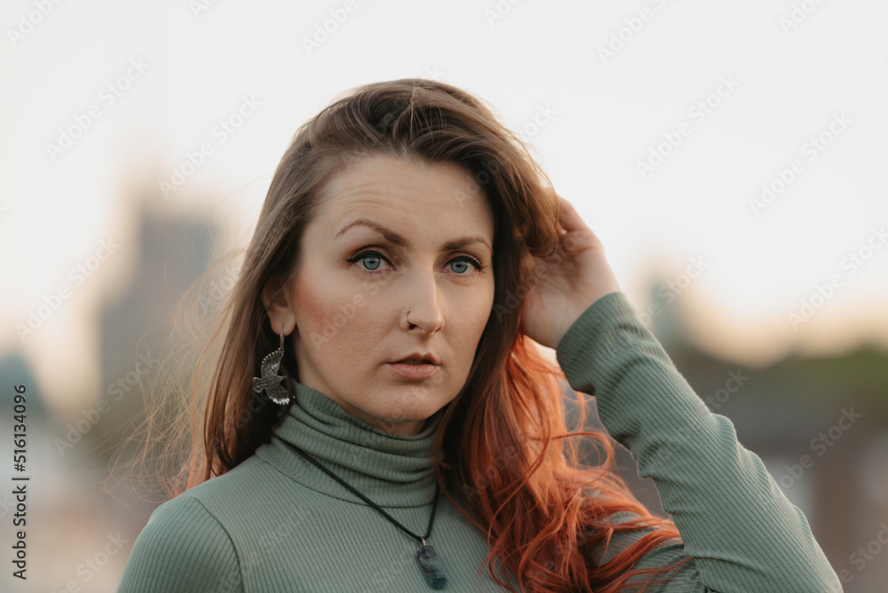 A close portrait of a redhead woman is staring into the distance with warsaw skyscrapers in the background at sunset. A close portrait of a redhead woman is staring into the distance with warsaw skyscrapers in the background at sunset.