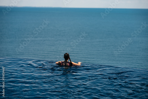 Happy woman in swimsuit swimming in infinity pool against seafront. © teksomolika