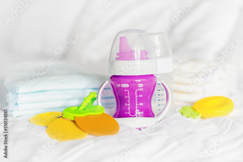 purple baby bottle of water disposable baby diapers toys on a white bed. Feeding complementary foods for a baby photo