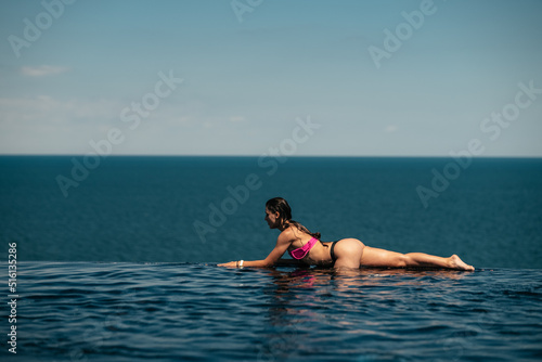 Happy woman in swimsuit swimming in infinity pool against seafront. © teksomolika