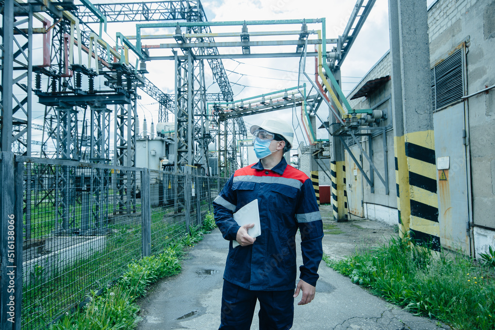 A masked power engineer during a pandemic inspects the modern equipment of an electrical substation before commissioning. Energy and industry. Scheduled repair of electrical equipment. A masked power engineer during a pandemic inspects the modern equipment of an electrical substation before commissioning. Energy and industry. Scheduled repair of electrical equipment.
