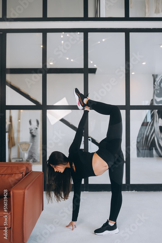 Young female wearing black sports suit stretching exercises indoors.