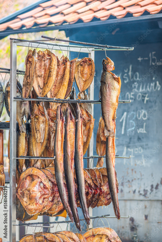 Hanging smoke-dried various fish in a fish market just smoked with hardwood wood chips in a smoker and ready to eat with info on a black board, vertical