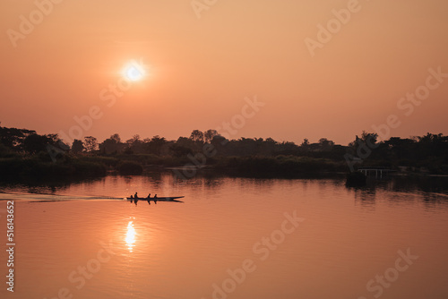 Don Det, Laos - January 19th, 2020 : fiery orange sunset on the Mekong river in Don Det, southern Laos with a boat on the water.