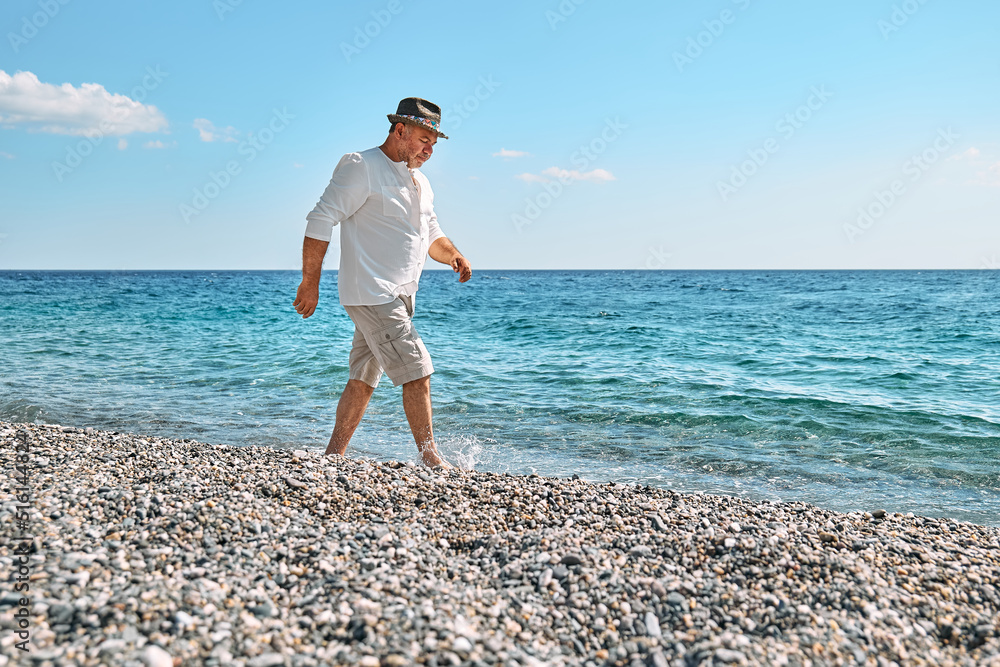 Happy middle-aged bearded man walking along beach. Concept of leisure activities, wellness, freedom, tourism, lifestyle and nature. Tourism in summertime.