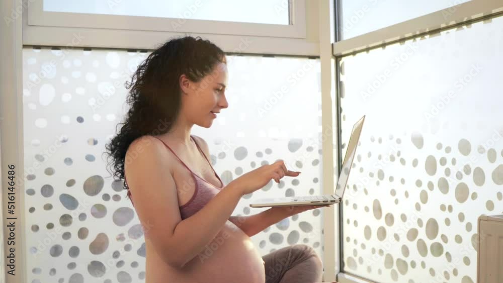 Pleasant pregnant young woman relaxing using laptop sitting on the floor near a big window. Pleasant pregnant young woman relaxing using laptop sitting on the floor near a big window.