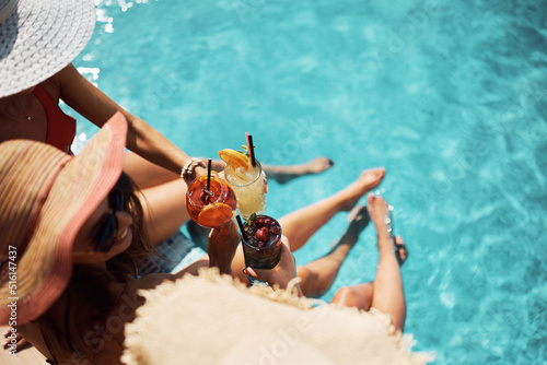 Close up of women toasting with cocktails while relaxing on summer day at the pool.