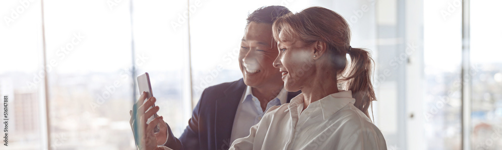 happy colleagues using smartphone for video call while standing near glass wall in modern office. happy colleagues using smartphone for video call while standing near glass wall in modern office.