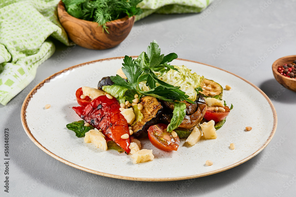 Salad with grilled vegetables, greens and cheese on concrete background. Warm salad with paprika, zucchini, eggplant and tomato on grill. Aesthetic composition with veggie salad. Summer menu concept. Salad with grilled vegetables, greens and cheese on concrete background. Warm salad with paprika, zucchini, eggplant and tomato on grill. Aesthetic composition with veggie salad. Summer menu concept.