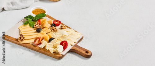 Cheese platter with nuts, honey sauce and olives on wood board. Cheeseboard on white concrete background. Cheese assorted in minimal style. Appetizers for wine. photo