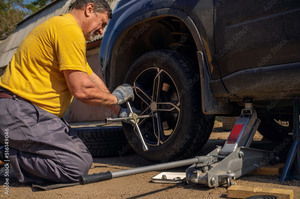 man in a yellow T-shirt changes the wheel of a car. Repair and replacement of wheels on a car with your own hands man in a yellow T-shirt changes the wheel of a car. Repair and replacement of wheels on a car with your own hands