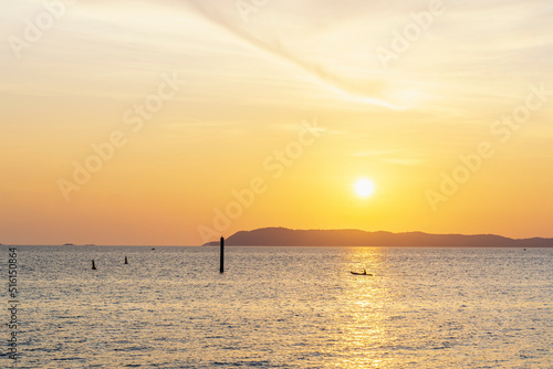 Colorful sunset shining over the bright orange waters of the ocean with a small ship floating. Silhouette of a small fishing boat on the sea at sunset. Soft focus on backgrounds of sundown.