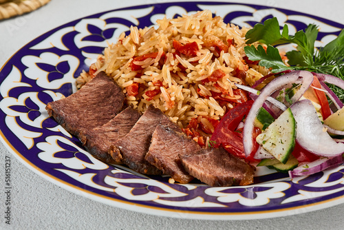 Traditional uzbek food - plov with beef. Eastern cuisine - pilaf with rice, meat and spices. Plov with beef on traditional uzbek plate. Composition of oriental ceramic plate with pilaf.